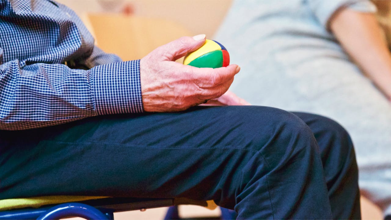 creative-02 Elderly man holding a colorful therapy ball indoors, promoting relaxation and health.