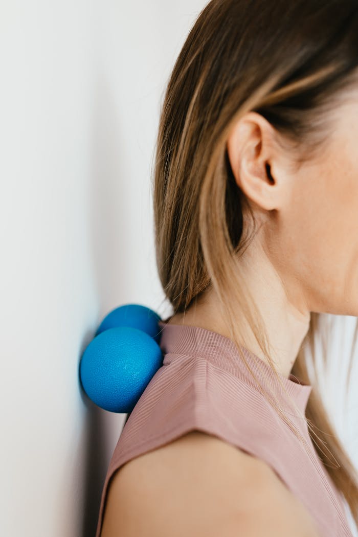 our-story Side view of a woman using blue massage balls against a wall for neck and shoulder tension relief.